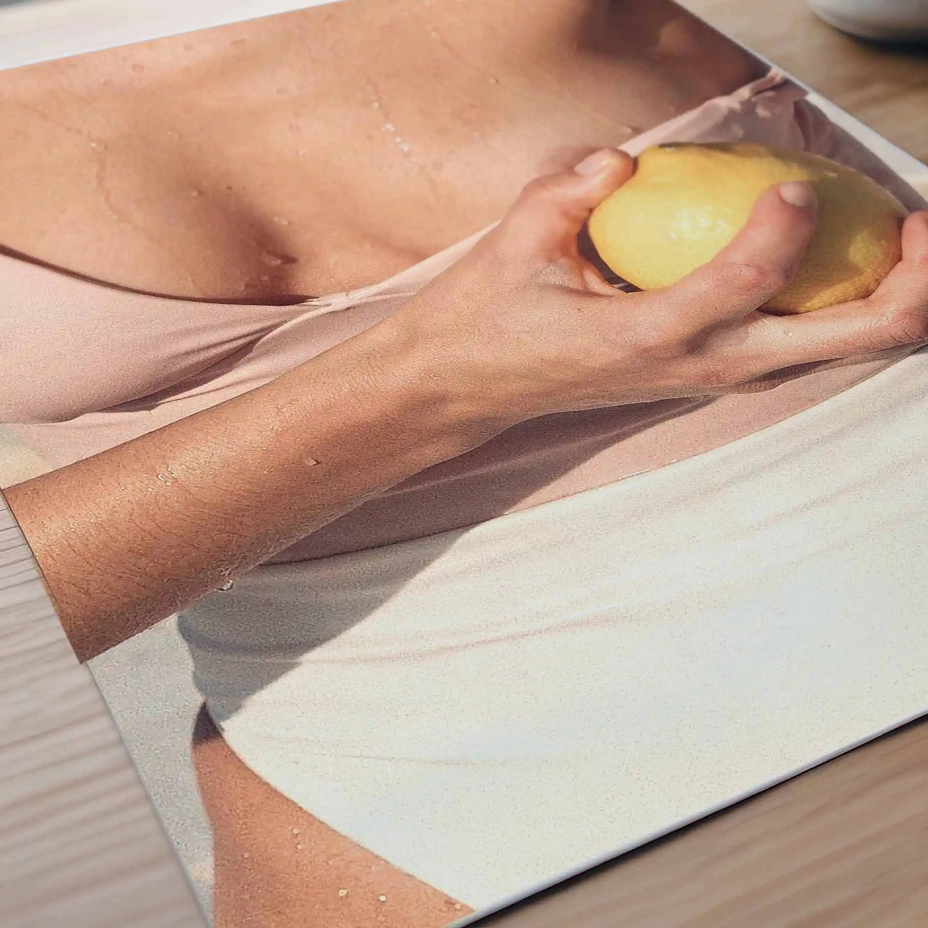 Editorial Mediterranean photography poster detail showing a fresh lemon held against sun-kissed skin with soft neutral tones and warm citrus colours.