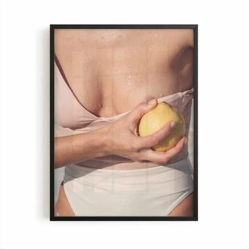 Editorial Mediterranean photography framed print showing a fresh lemon held against sun-kissed skin with soft neutral tones and warm citrus colours.