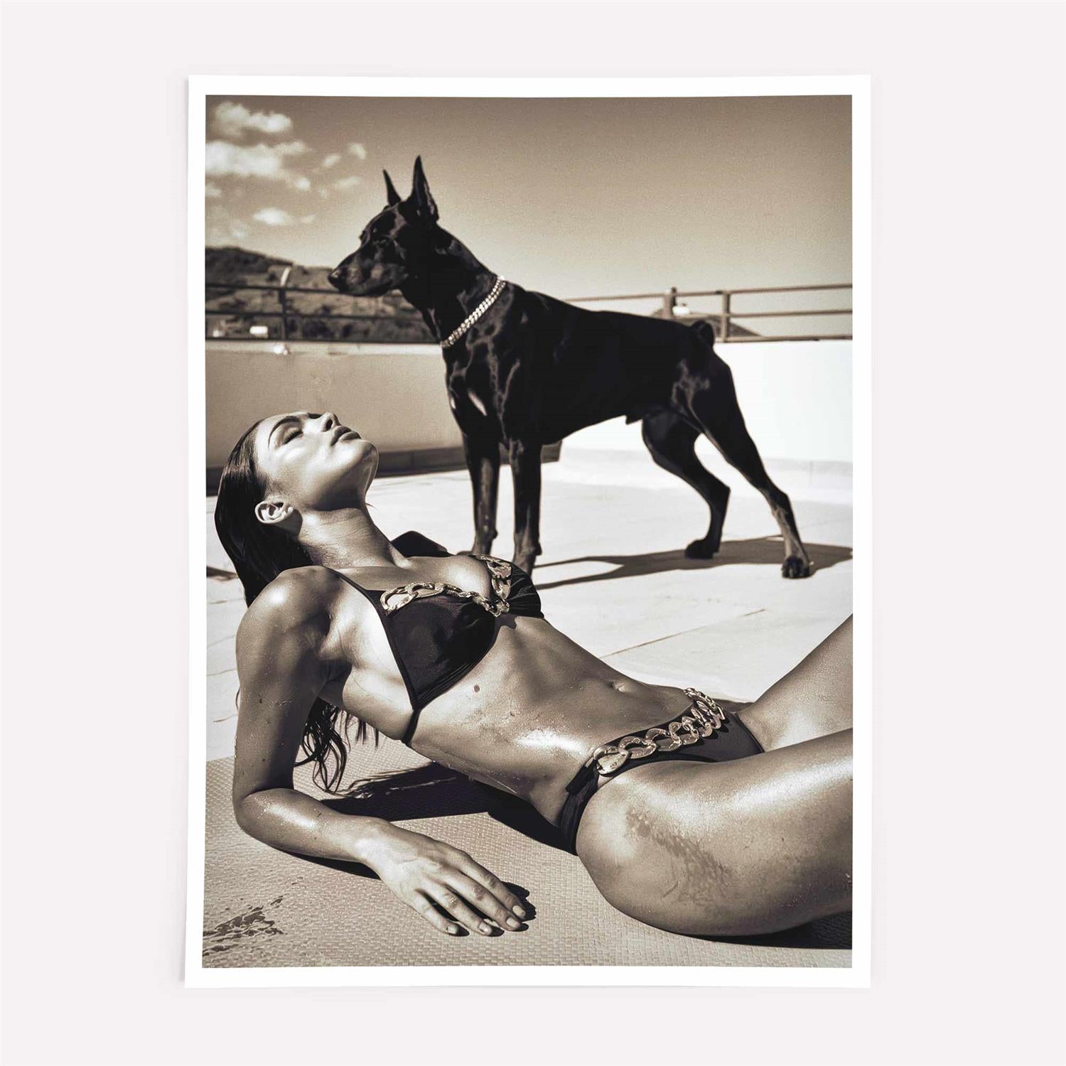 Woman in a bikini lying on the beach with a dog standing nearby on print only