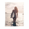 Surfer girl walking into the ocean at golden hour carrying a surfboard during sunset, creating a peaceful coastal photography fine art print