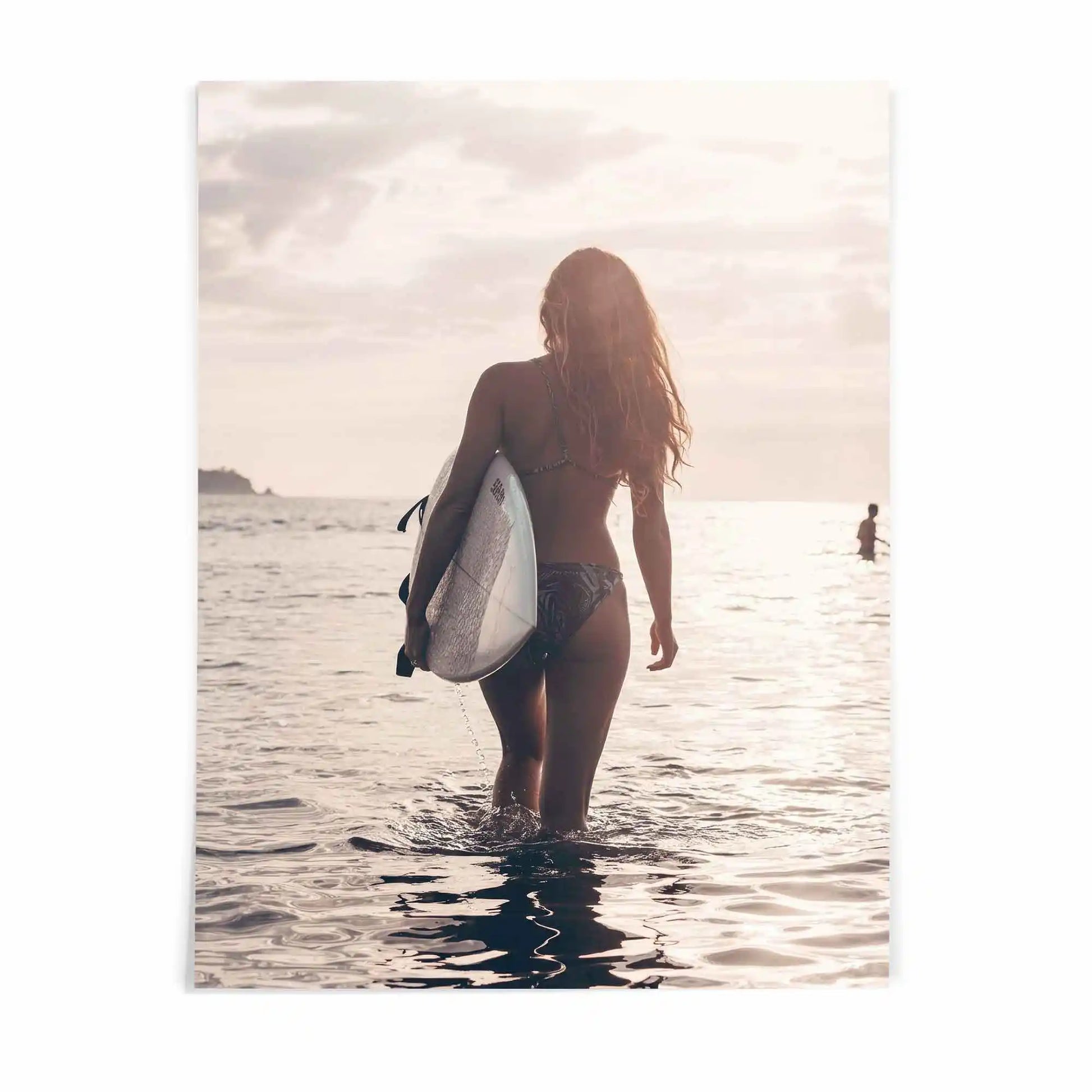 Surfer girl walking into the ocean at golden hour carrying a surfboard during sunset, creating a peaceful coastal photography fine art print